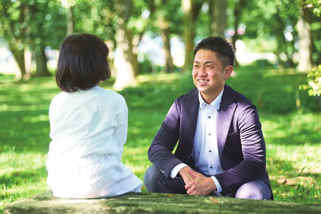 公園の芝生で娘と向き合い笑顔で話す佐藤和幸